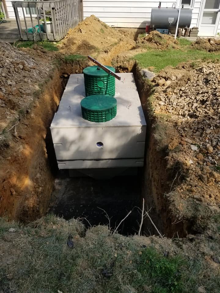 Concrete septic tank with green access risers set in an excavated trench beside a house